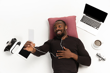 Image showing Emotional african-american man using phone surrounded by gadgets isolated on white studio background, technologies connecting people. Online meeting, selfie