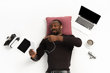 Image showing Emotional african-american man using phone surrounded by gadgets isolated on white studio background, technologies connecting people. Selfie