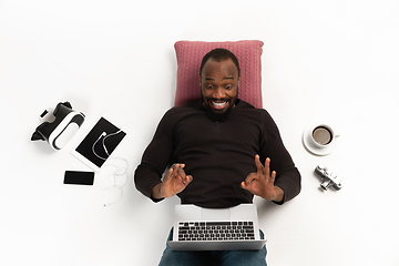 Image showing Emotional african-american man using laptop surrounded by gadgets isolated on white studio background, technologies. Showing nice