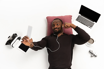 Image showing Emotional african-american man using phone surrounded by gadgets isolated on white studio background, technologies connecting people. Online meeting, selfie