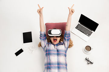 Image showing Emotional caucasian woman using VR-headsed, surrounded by gadgets isolated on white studio background, technologies. Happy winning