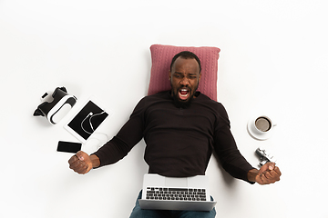 Image showing Emotional african-american man using laptop surrounded by gadgets isolated on white studio background, technologies. Winning