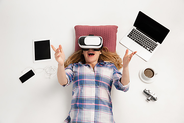 Image showing Emotional caucasian woman using VR-headsed, surrounded by gadgets isolated on white studio background, technologies. Happy, greeting