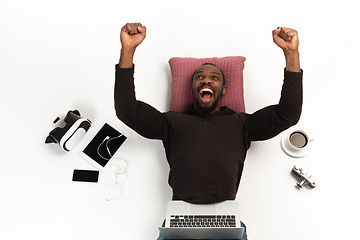 Image showing Emotional african-american man using laptop surrounded by gadgets isolated on white studio background, technologies. Crazy winning