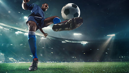 Image showing Football or soccer player in action on stadium with flashlights, kicking ball for winning goal, wide angle. Action, competition in motion