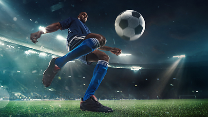 Image showing Football or soccer player in action on stadium with flashlights, kicking ball for winning goal, wide angle. Action, competition in motion
