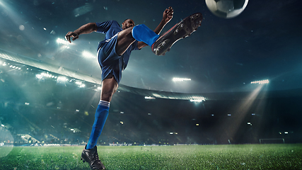 Image showing Football or soccer player in action on stadium with flashlights, kicking ball for winning goal, wide angle. Action, competition in motion