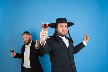 Image showing Portrait of a young orthodox jewish men isolated on blue studio background, meeting the Passover, eating Aman\'s ears with wine