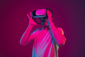 Image showing Caucasian man\'s portrait isolated on pink-purple studio background in neon light, playing with VR-headset