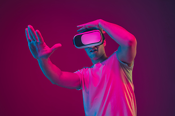 Image showing Caucasian man\'s portrait isolated on pink-purple studio background in neon light, playing with VR-headset