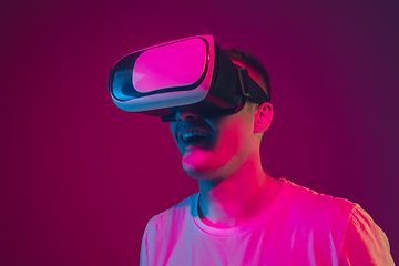 Image showing Caucasian man\'s portrait isolated on pink-purple studio background in neon light, playing with VR-headset