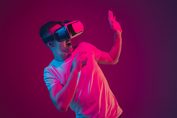 Image showing Caucasian man\'s portrait isolated on pink-purple studio background in neon light, playing with VR-headset