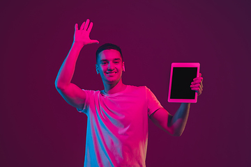 Image showing Caucasian man\'s portrait isolated on pink-purple studio background in neon light, using tablet