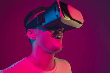 Image showing Caucasian man\'s portrait isolated on pink-purple studio background in neon light, playing with VR-headset