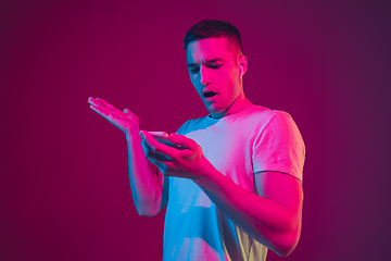 Image showing Caucasian man\'s portrait isolated on pink-purple studio background in neon light, with smartphone and earphones