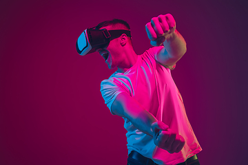 Image showing Caucasian man\'s portrait isolated on pink-purple studio background in neon light, playing with VR-headset