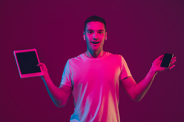 Image showing Caucasian man\'s portrait isolated on pink-purple studio background in neon light, using tablet