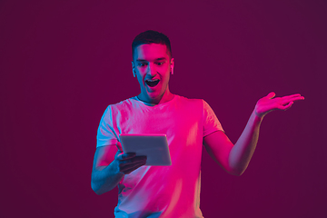 Image showing Caucasian man\'s portrait isolated on pink-purple studio background in neon light, using tablet