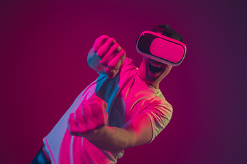 Image showing Caucasian man\'s portrait isolated on pink-purple studio background in neon light, playing with VR-headset