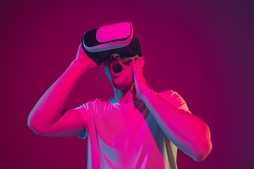 Image showing Caucasian man\'s portrait isolated on pink-purple studio background in neon light, playing with VR-headset