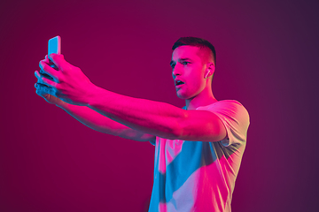 Image showing Caucasian man\'s portrait isolated on pink-purple studio background in neon light, with smartphone and earphones