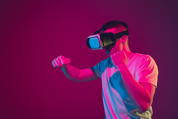 Image showing Caucasian man\'s portrait isolated on pink-purple studio background in neon light, playing with VR-headset