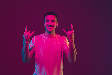 Image showing Caucasian man\'s portrait isolated on pink-purple studio background in neon light, using wireless earphones