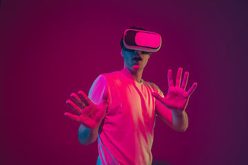 Image showing Caucasian man\'s portrait isolated on pink-purple studio background in neon light, playing with VR-headset