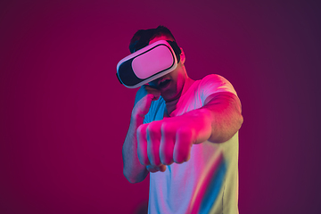 Image showing Caucasian man\'s portrait isolated on pink-purple studio background in neon light, playing with VR-headset