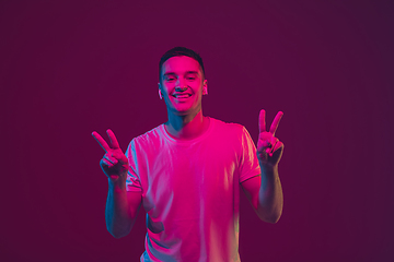 Image showing Caucasian man\'s portrait isolated on pink-purple studio background in neon light, using wireless earphones