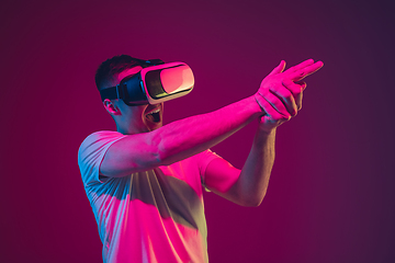 Image showing Caucasian man\'s portrait isolated on pink-purple studio background in neon light, playing with VR-headset