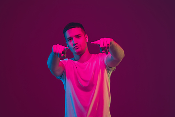 Image showing Caucasian man\'s portrait isolated on pink-purple studio background in neon light, using wireless earphones