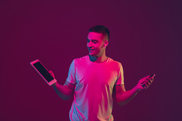 Image showing Caucasian man\'s portrait isolated on pink-purple studio background in neon light, using tablet