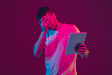 Image showing Caucasian man\'s portrait isolated on pink-purple studio background in neon light, using tablet