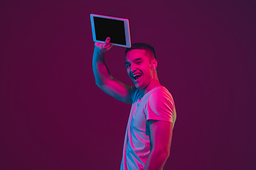 Image showing Caucasian man\'s portrait isolated on pink-purple studio background in neon light, using tablet