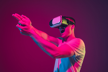 Image showing Caucasian man\'s portrait isolated on pink-purple studio background in neon light, playing with VR-headset