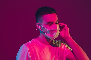 Image showing Caucasian man\'s portrait isolated on pink-purple studio background in neon light, wearing face mask