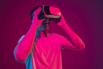 Image showing Caucasian man\'s portrait isolated on pink-purple studio background in neon light, playing with VR-headset