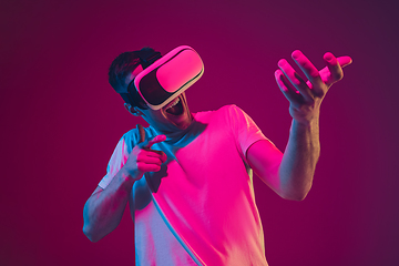 Image showing Caucasian man\'s portrait isolated on pink-purple studio background in neon light, playing with VR-headset