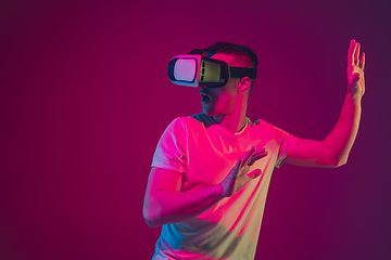 Image showing Caucasian man\'s portrait isolated on pink-purple studio background in neon light, playing with VR-headset