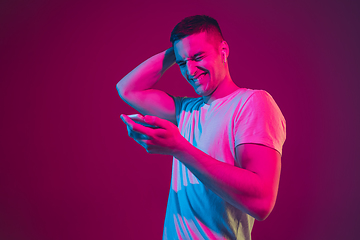 Image showing Caucasian man\'s portrait isolated on pink-purple studio background in neon light, with smartphone and earphones