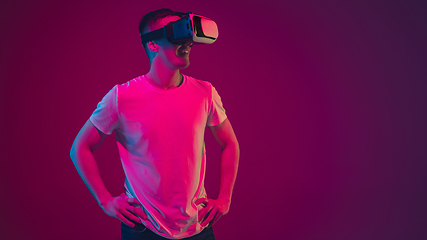 Image showing Caucasian man\'s portrait isolated on pink-purple studio background in neon light, playing with VR-headset