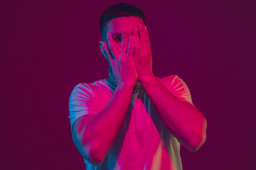 Image showing Caucasian man\'s portrait isolated on pink-purple studio background in neon light, using wireless earphones