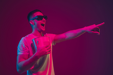 Image showing Caucasian man\'s portrait isolated on pink-purple studio background in neon light, wearing 3D-cinema eyewear