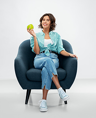 Image showing happy woman with green apple sitting in armchair