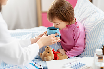 Image showing doctor giving hot tea to sick little girl in bed