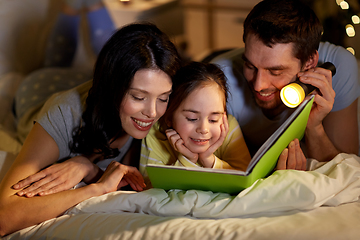 Image showing happy family reading book in bed at night at home