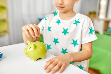 Image showing little boy putting coin into piggy bank at home