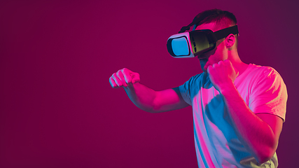 Image showing Caucasian man\'s portrait isolated on pink-purple studio background in neon light, playing with VR-headset