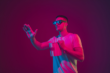 Image showing Caucasian man\'s portrait isolated on pink-purple studio background in neon light, wearing 3D-cinema eyewear